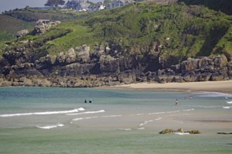 Small waves rolling towards a sandy beach with rocks, people enjoying the water, St Ives, Cornwall,