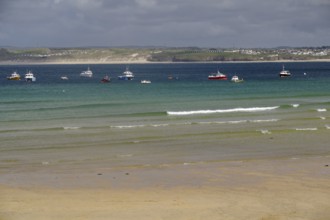 Several boats floating on a calm sea in front of a misty coastline, St Ives, Cornwall, England,