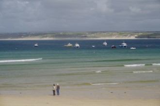 Boats anchored on calm waters off a wide, deserted sandy beach, St Ives, Cornwall, England, United