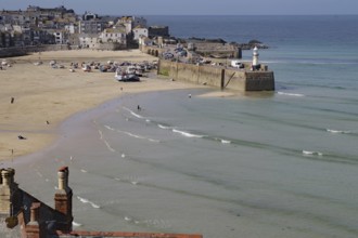 Coastal town with harbour and lighthouse, boats on the beach and gentle waves in the blue sea,