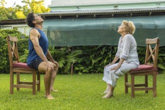 Senior woman and personal trainer engaging in seated exercises on chairs in a serene garden,