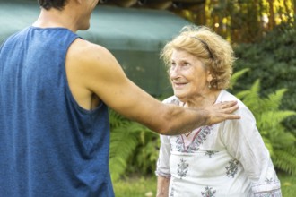 Young physiotherapist supporting and comforting smiling elderly woman during rehabilitation session