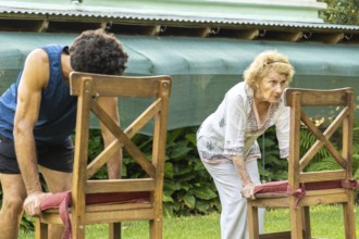 Senior woman and her personal trainer bending over while gripping chairs, engaging in back muscle