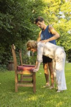 Physiotherapist is assisting a senior woman performing bending exercises with the help of a chair