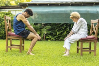 Senior woman and her physiotherapist are performing physical therapy exercises sitting on chairs in