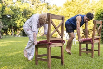 Senior woman and her physiotherapist are performing a rehabilitation exercise using chairs in a