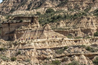 Group of hikers at colorful sandstone rock formations, desert, along gravel road Ruta Jubierre,