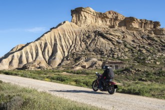 Biker riding motorcycle, gravel road, colorful rock formation, semi-desert, Bardena Blanca area,