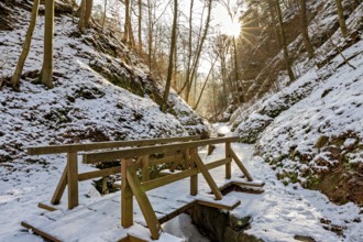 Wooden bridge over a snow-covered path in a sunny winter forest, The Dragon Gorge near Eisenach in