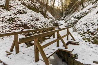 Narrow wooden bridge over a frozen stream in a snowy forest gorge at sunset, The Dragon Gorge near