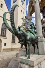 Bronze sculpture of a horseman next to a church with a tower and artistic arches in the background,