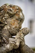 Close-up of a weathered stone sculpture of a head covered in moss, stone statues in the town of