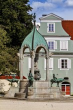 Historic fountain with green dome in front of a building with white windows in summer, The fountain