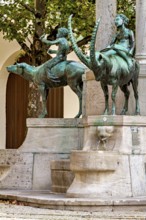 Bronze figures of riders on animals at an ornate fountain with arched structures, The fountain in