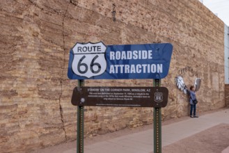 Woman posing for a photo behind roadside attraction sign at Standin' on the Corner Park in downtown