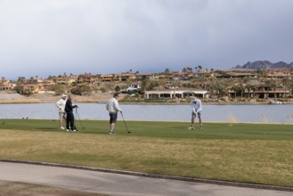 Foursome of senior golfers teeing off while playing on a golf course along the shoreline of Las