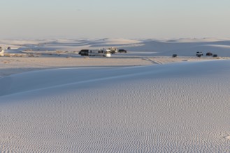 Cars and RVs in a parking area behind a rippled white gypsum sand dune at White Sands National Park