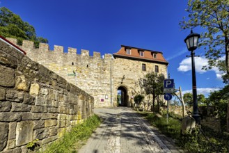 Stone entrance to a castle with cobblestone street and blue sky in the background, The Creuzburg in