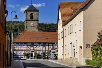 Church tower towers above half-timbered house and village street in sunny weather, The church tower