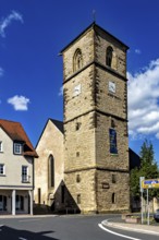 Historic stone church tower with clock in front of a blue sky, surrounded by modern buildings, The