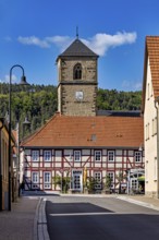 A half-timbered house with a church tower in the village, shining under a blue sky, The church