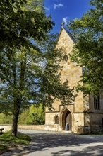 A Gothic church made of sandstone surrounded by trees under a bright blue sky, the Liborius Chapel