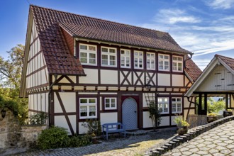 A traditional half-timbered house with red roof tiles and bench in a sunny rural courtyard,