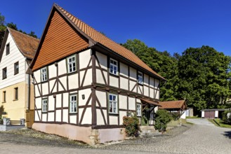 A picturesque half-timbered house with red roof tiles under a bright blue sky in the countryside,