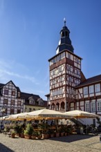 Historic half-timbered building with tower and sunshades on a market square under a clear blue sky,