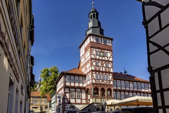 Half-timbered tower and surrounding buildings, seen through a narrow alley under a blue sky, The