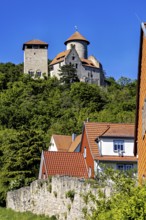 Half-timbered houses with red roofs in front of a castle on a wooded hill, Normannstein Castle near