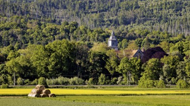 Landscape with church in the forest background and hay bales in the foreground, The church tower of