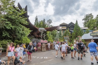 Park guests walk past a large steel sculpture of an eagle near the Wild Eagle wing roller coaster