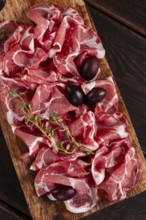 Freshly cut dried meat, served with olives and herbs, on a wooden chopping board, no people