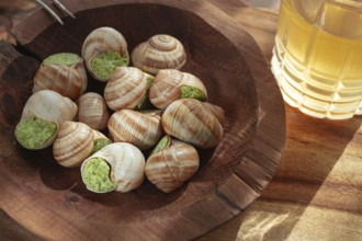 Snails cooked with herb oil on a wooden plate, served with white wine, natural light, no people