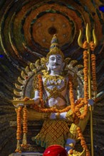 Hindu deity Shiva holding a trident, offerings in the foreground, a cosmic symbol in the back,