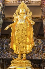 Gilded Buddha statue standing on a gilded base, Buddhist temple complex Wat Phra That Sorn Kaew,