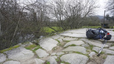 A hiking backpack and hiking sticks on stone slabs of a bridge, making a pilgrimage on the Caminho