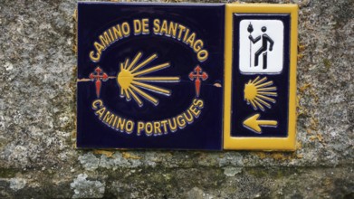 Guide on the Camino de Santiago with yellow arrow symbolism and cross, scallop on a stone wall,