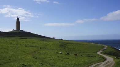 Coast with lighthouse and green field under a blue sky with clouds and a path to the sea, A Coruna,