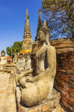Stone Buddha statues sitting in a row, two temple towers in the back, Prang, historic Buddhist