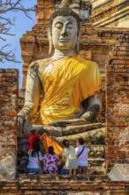 A family decorates a stone Buddha statue with yellow cloth, historic Buddhist temple complex,