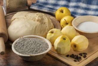 Dough with peeled apples, poppy seeds, sugar and raisins on a wooden table