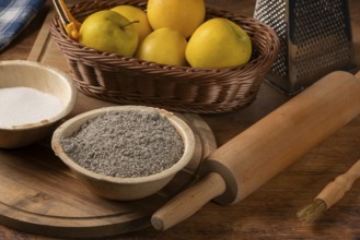 Basket with apples, bowl with poppy seeds and rolling pin on a rustic wooden table