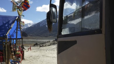 A bus and a colorful tent with pennants against a mountain backdrop, snack at a kiosk on a plateau