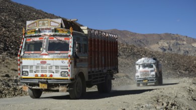 Two traditionally painted Indian trucks drive on a dusty, mountainous Manali-Leh Highway, Himachal