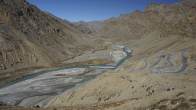 Shimmering blue Indus meanders through a barren valley with serpentines of a road leading down to