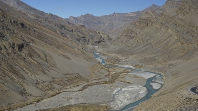 Shimmering blue Indus meanders through a barren valley under a blue sky, trekking in Ladakh,