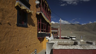 Façade of a Buddhist monastery casting shadows against a clear sky and mountain landscape, trekking