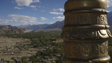 Detail of a golden prayer wheel against the backdrop of a vast mountain landscape, view of the